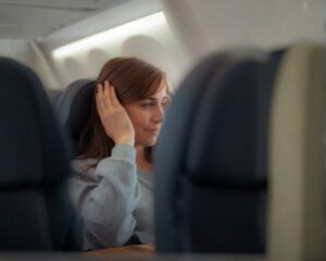 Eine Passagierin im Flugzeug leidet unter Ohrendruck während des Flugs und greift sich ans Ohr.